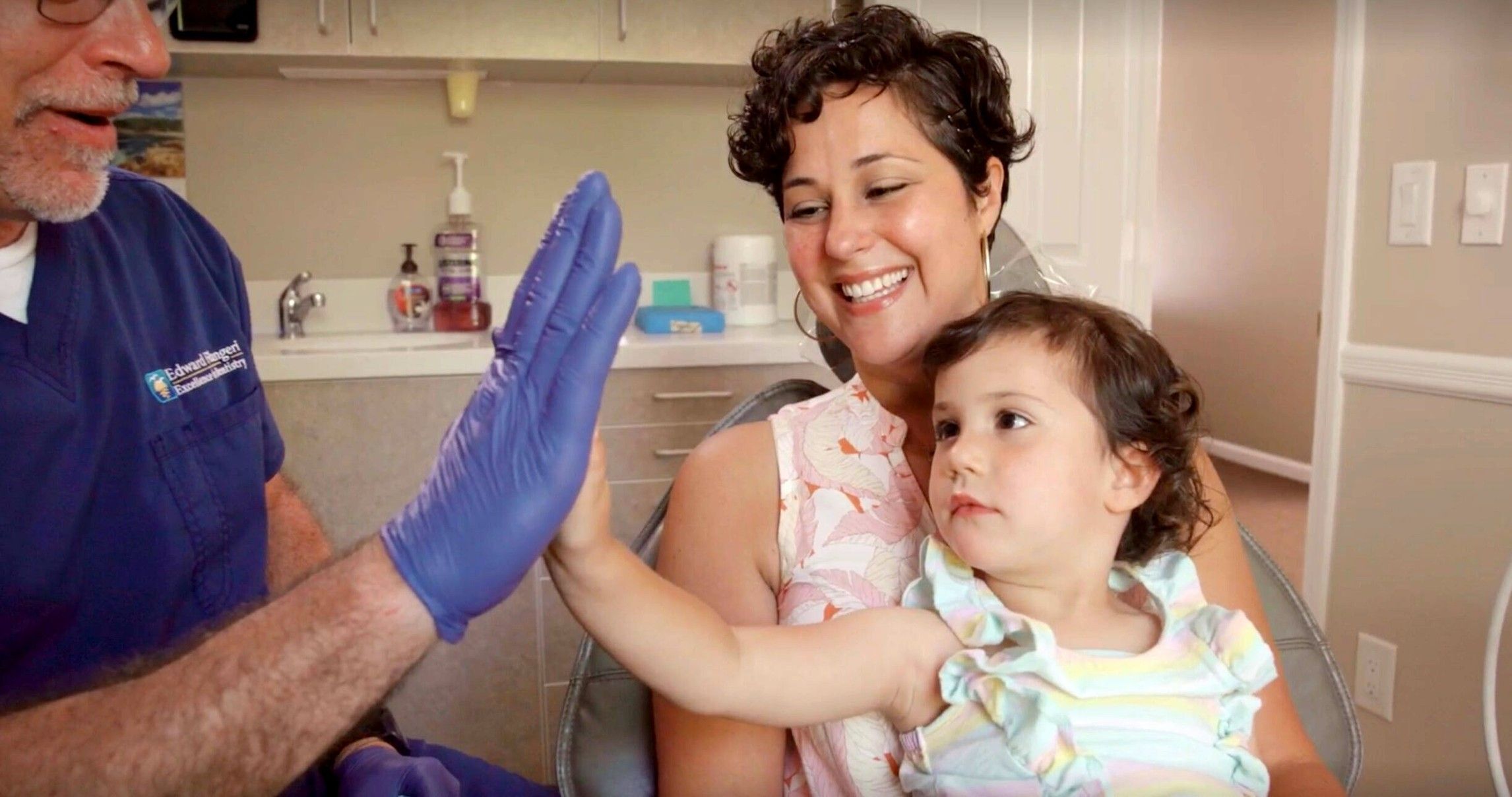 Dr. Ed high-fiving a toddler on her mother's lap