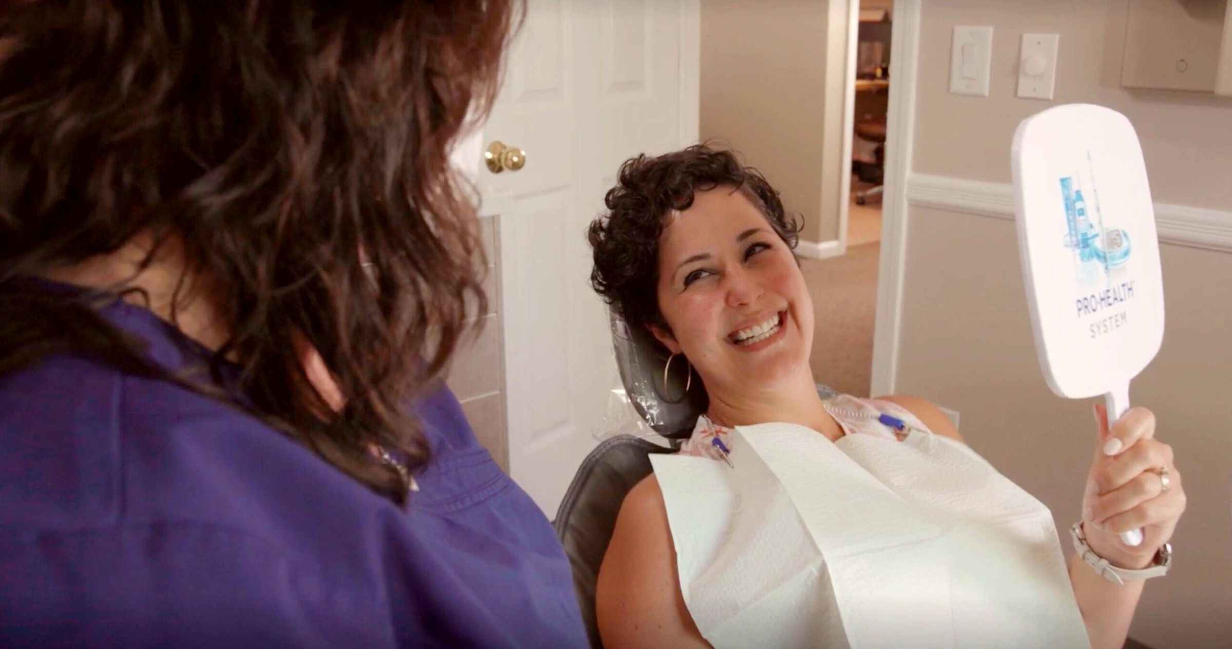 A patient smiling at her teeth in a hand mirror